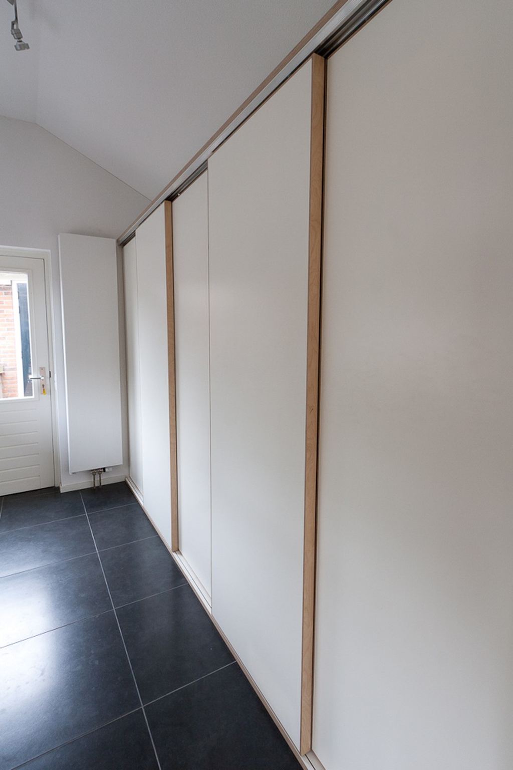 Rij witte schuifdeuren van een kast, met smalle houten stroken tussen de panelen.