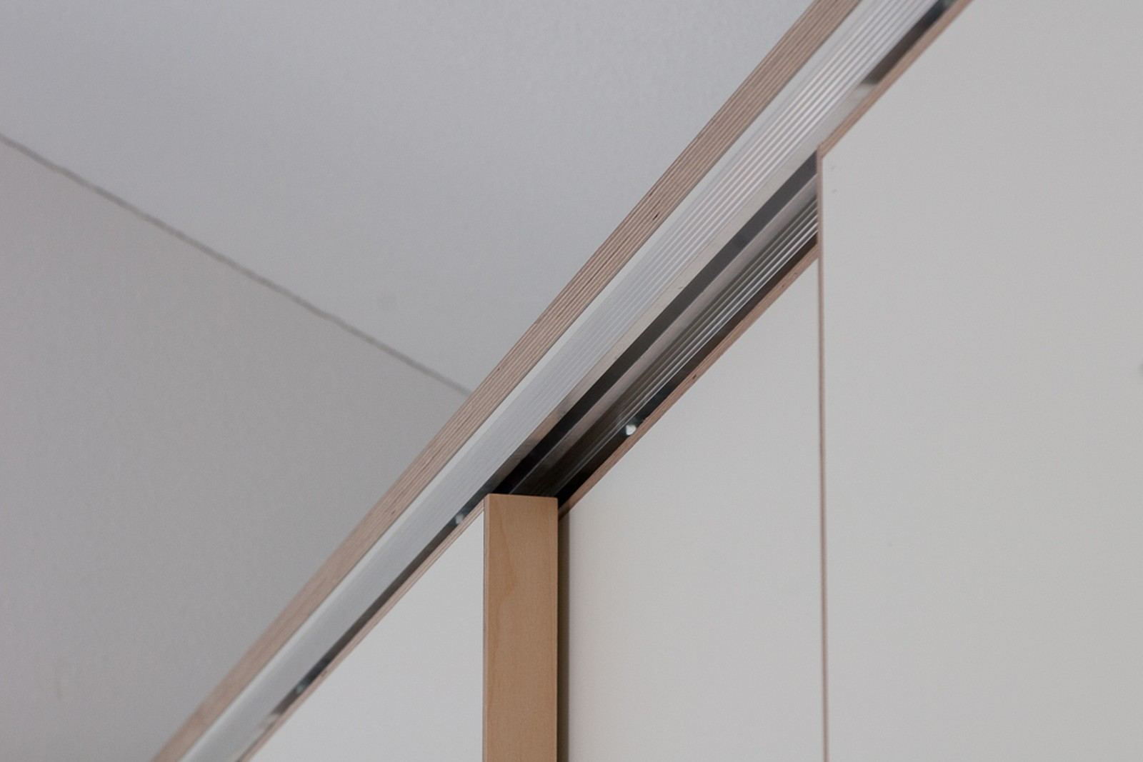 Detail van de bovenrail van een schuifdeurkast, met een lichte plaatrand tegen de wand.