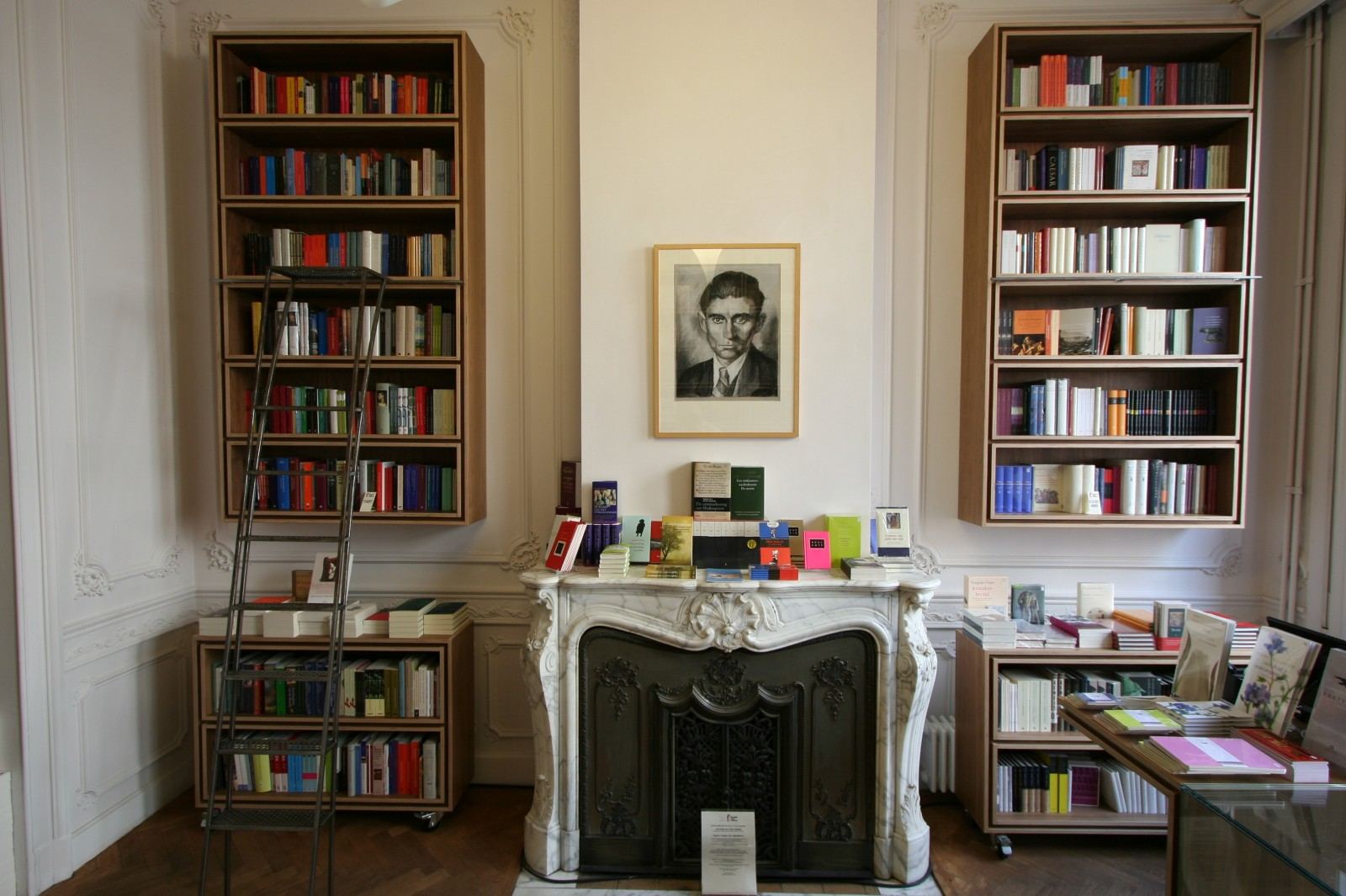 Twee notenfineer boekenkasten naast de schouw, met een rolladder.