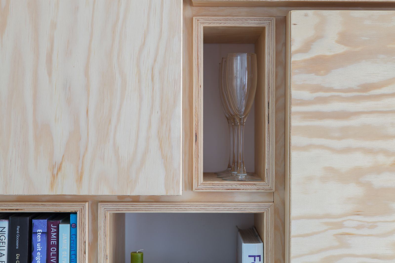 Open vakken van de wandkast met een wijnglas en boeken.
