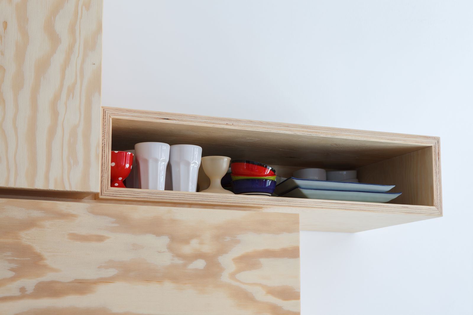 Open vak van de wandkast met kopjes, kommetjes en bordjes.