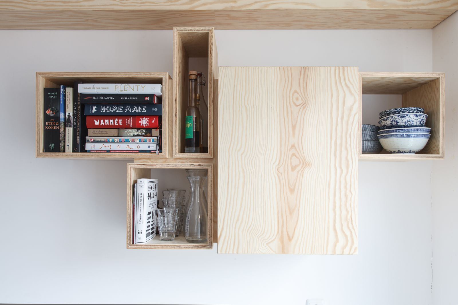 Wandkast van grenen multiplex met open en gesloten vakken vol kookboeken.