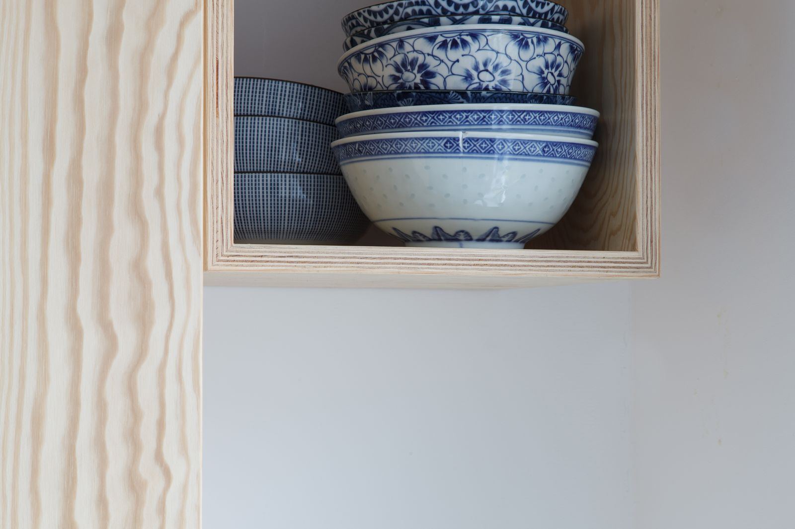 Open vak van de wandkast met een stapel blauw-wit gedecoreerde kommen.