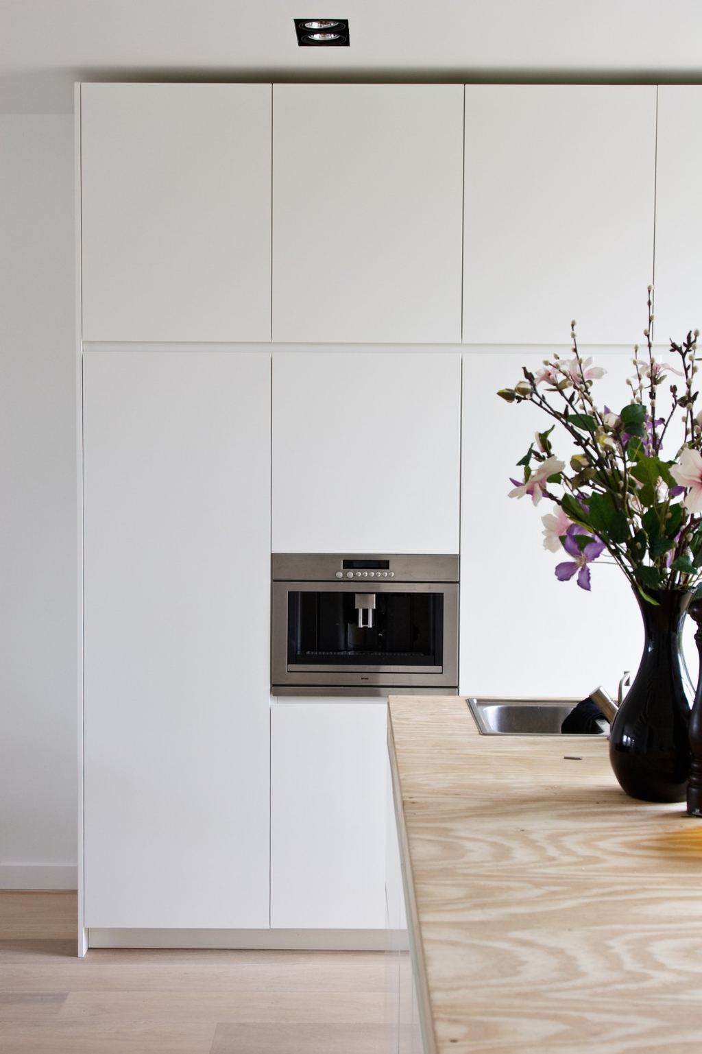 Hoge witte kastenwand met ingebouwde koffiemachine boven het vuren aanrechtblad.
