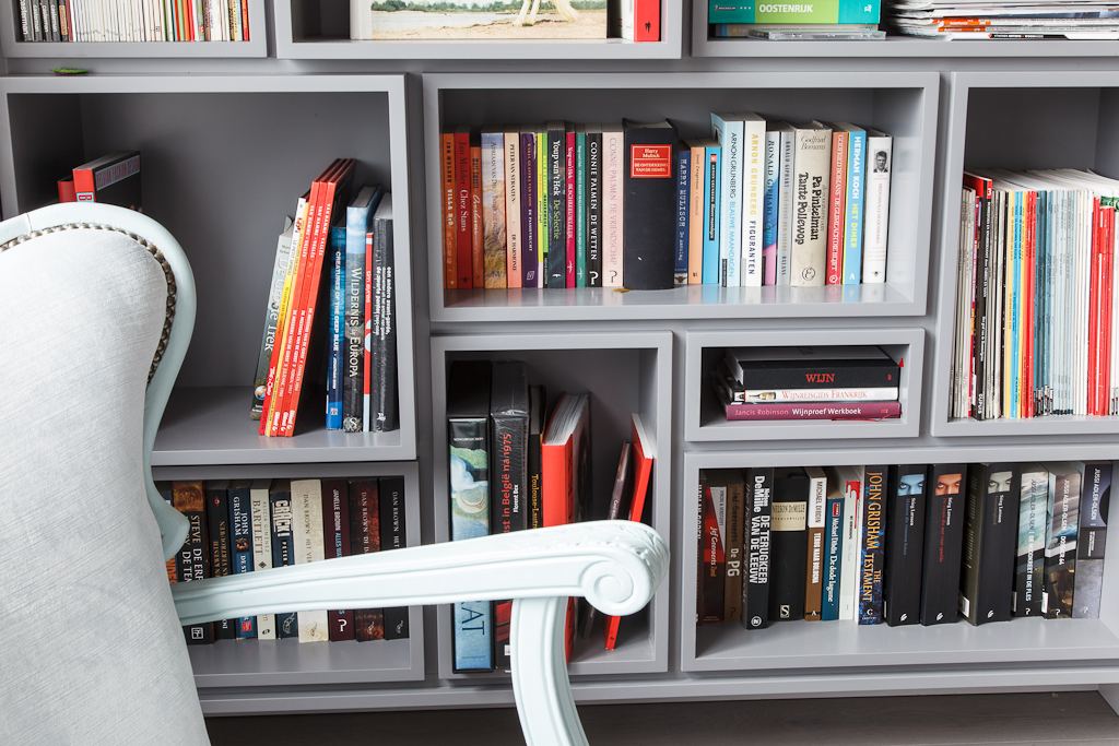 Wandvullende grijze boekenkast met ondiepe en diepe vakken naast elkaar.