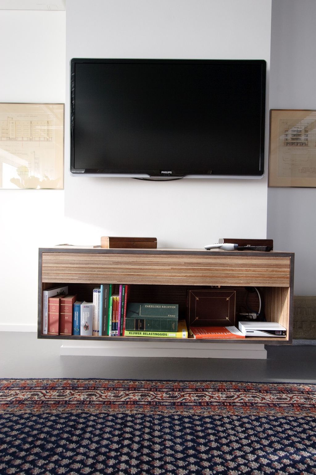 Zwevend tv-meubel met open boekenvak onder een wandgemonteerde televisie.