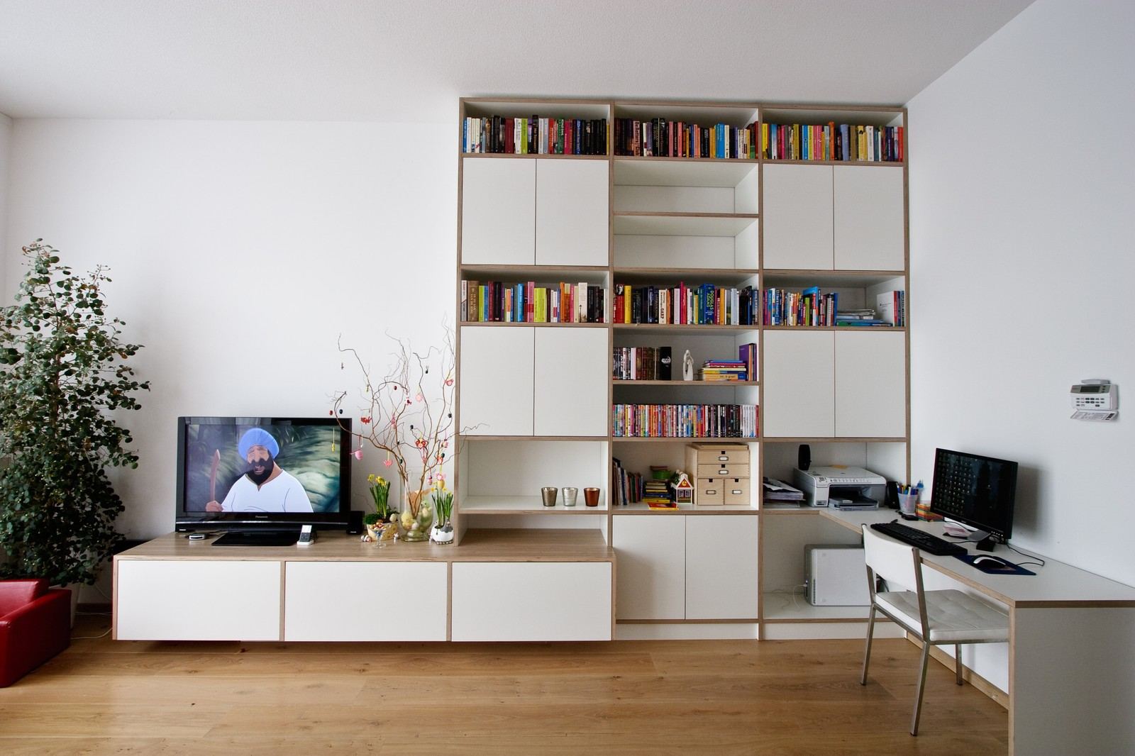 Boekenkast met witte deuren naast een bureau en tv-meubel.
