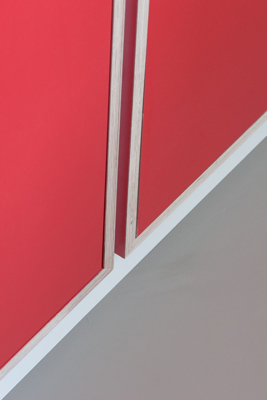 Detail van de rode kastdeuren boven een witte plint.