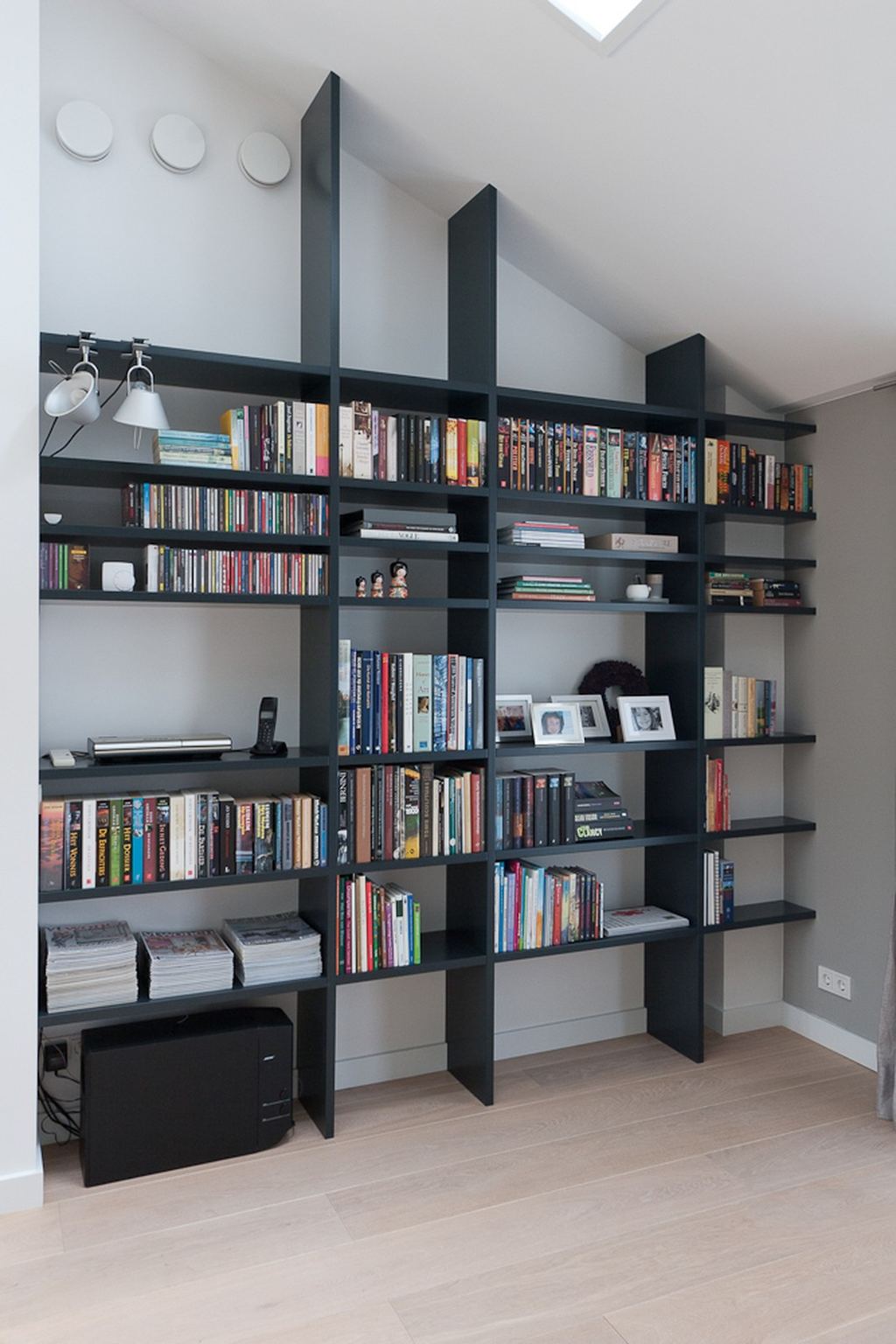 Zwarte boekenkast met een minimalistisch lijnenspel tegen het schuine plafond.