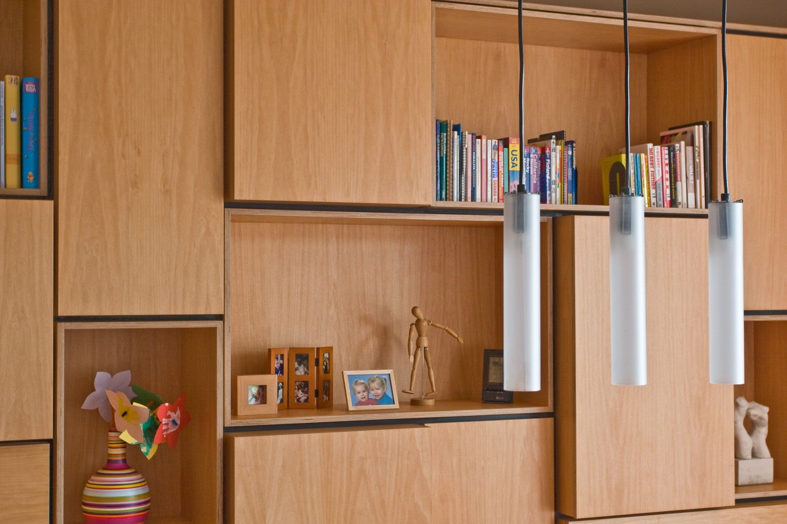 Open vakken met boeken, een houten mannequin en fotolijstjes.