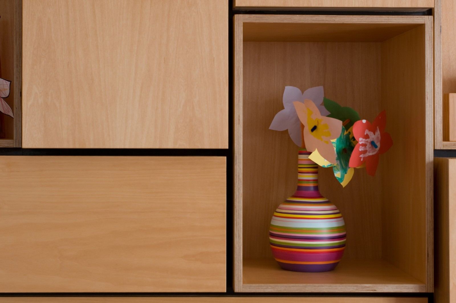 Gestreepte vaas met papieren bloemen in een open kastvak.
