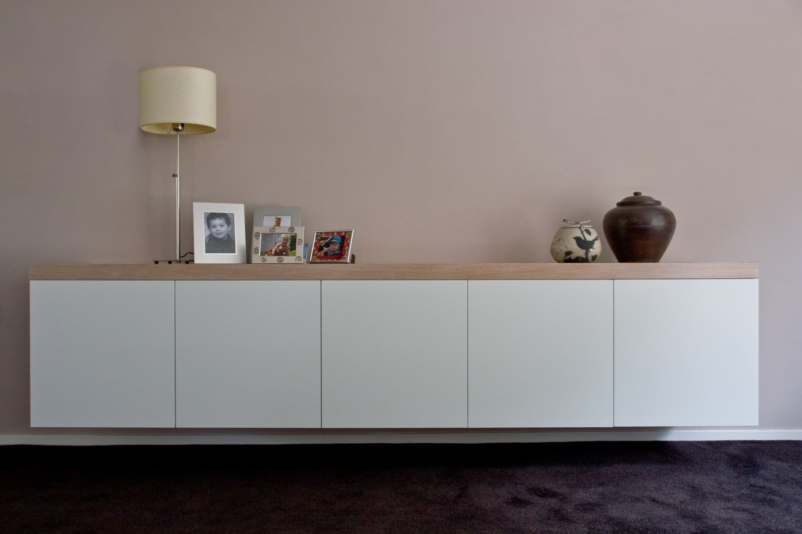 Lang zwevend dressoir met vijf witte deurpanelen en een licht houten bovenrand.