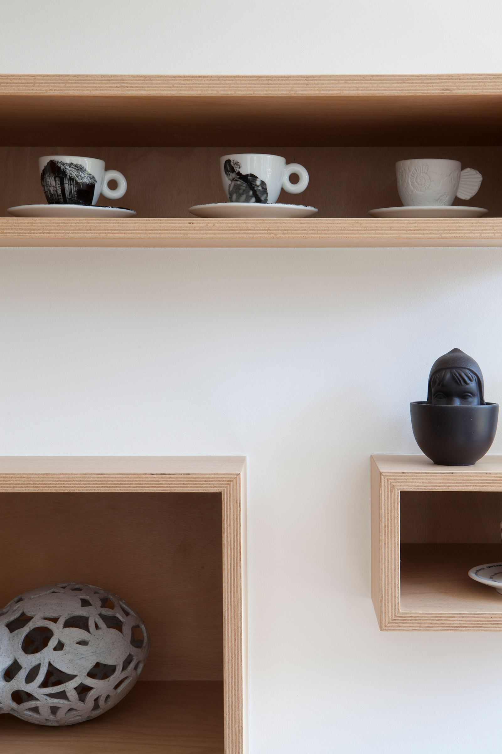 Detail van twee berken multiplex vakken met espressokopjes en beeldjes.